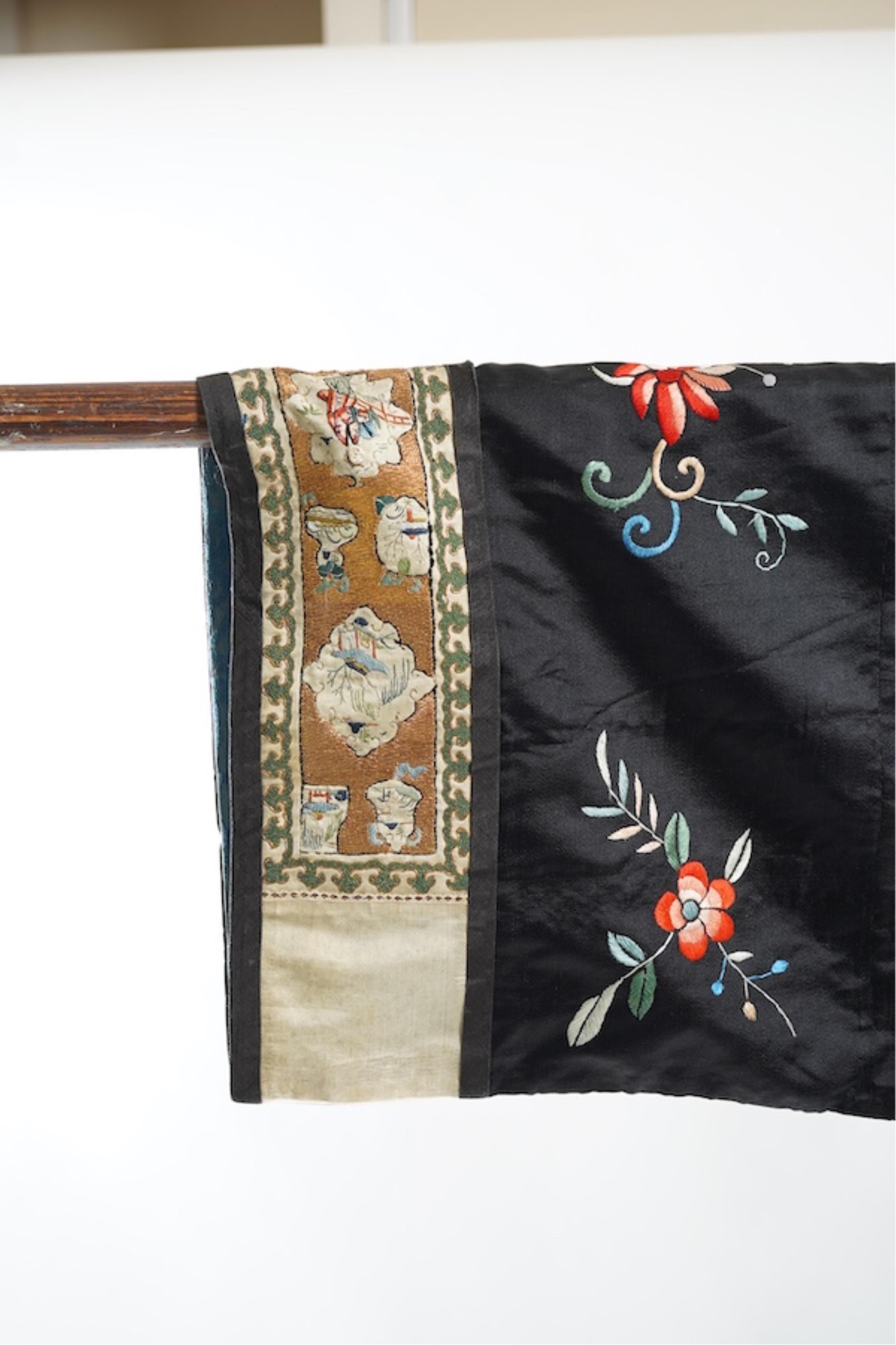 A late 19th early 20th century Chinese black silk polychrome embroidered ladies robe, decorated with cream silk, gilt and Peking knot bordered sleeve bands. The sleeve bands worked with fine figural and other embroidered